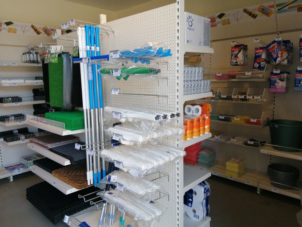 Store aisle with mops, brooms, and cleaning supplies on pegboard shelves.