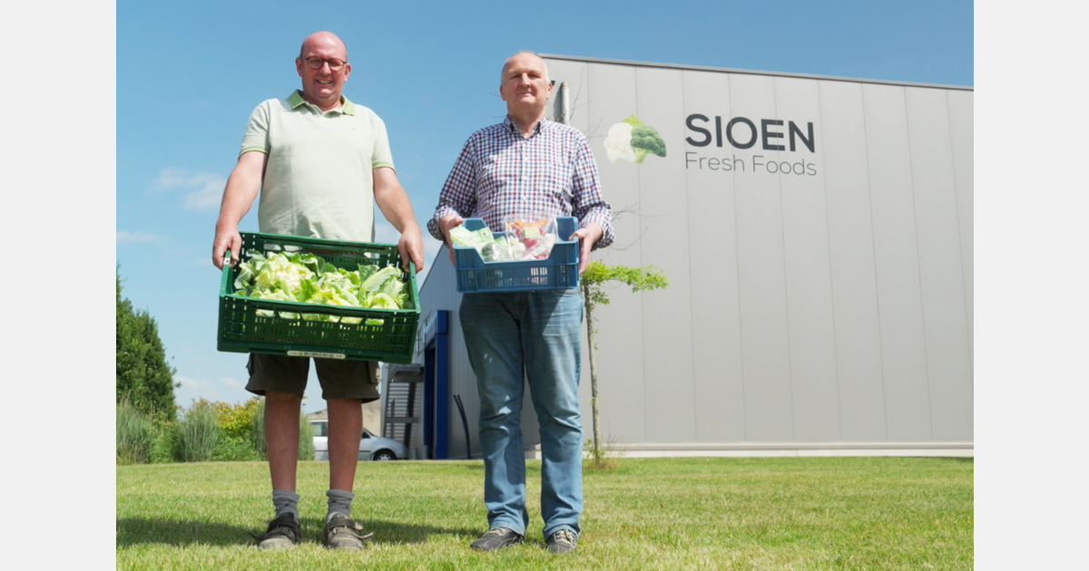 Two men stand on a lawn outside a SIOEN Fresh Foods building, each holding a crate of fresh vegetables.