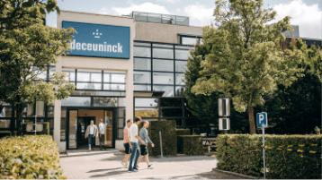 Office building with a blue Deceuninck sign, glass front, trees, and people walking toward the entrance.